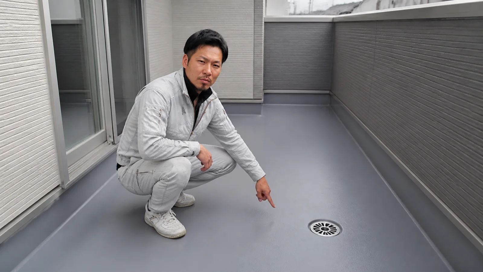 ベランダの防水床と排水口を坂本さんが確認する場面